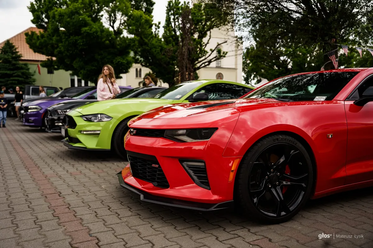Rząd amerykańskich muscle carów: na pierwszym planie czerwony Chevrolet Camaro SS, za nim zielony Ford Mustang, ciemny Ford Mustang oraz fioletowy Dodge Charger.