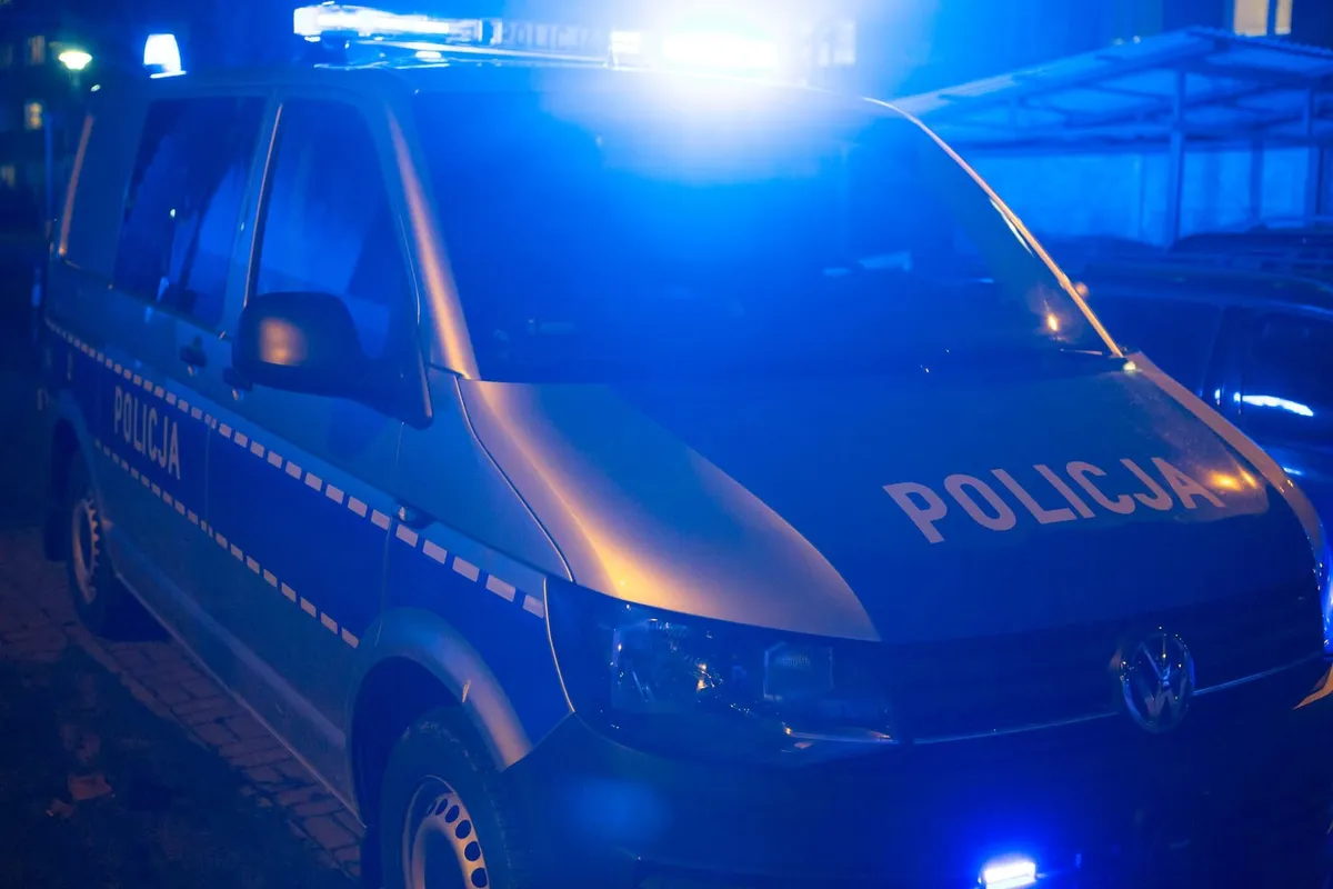 radiowóz volkswagen polskiej policji z włączonymi niebieskimi sygnałami w nocy